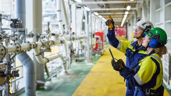 Two employees in high vis gear pointing at some pipes 